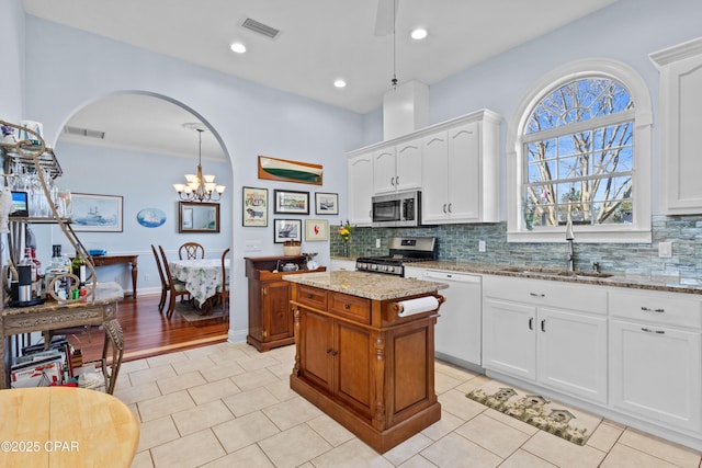 kitchen featuring stainless steel appliances, white cabinets, a kitchen island, and light stone counters