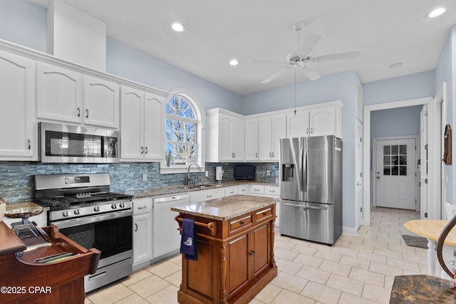 kitchen featuring white cabinets, a kitchen island, light stone countertops, stainless steel appliances, and a sink