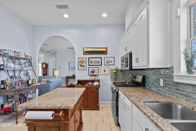 kitchen with arched walkways, stainless steel appliances, decorative backsplash, white cabinets, and light stone countertops