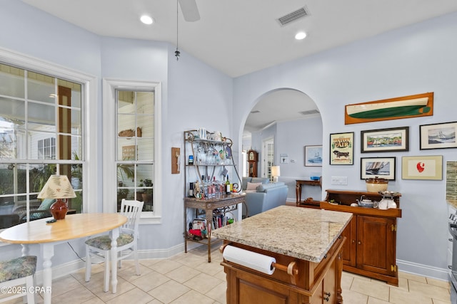 kitchen featuring arched walkways, brown cabinets, light tile patterned floors, visible vents, and baseboards