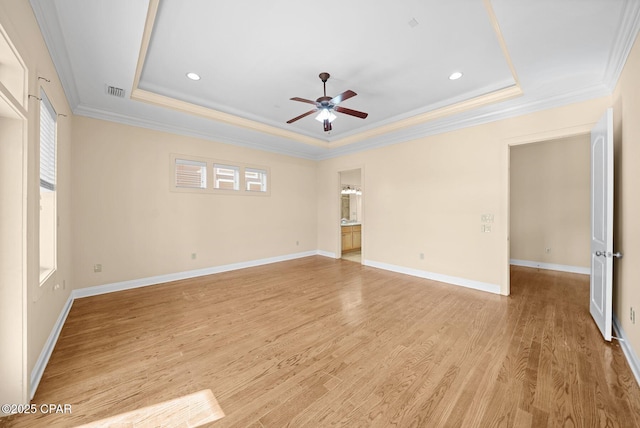 empty room featuring a tray ceiling, light hardwood / wood-style flooring, ornamental molding, and a wealth of natural light