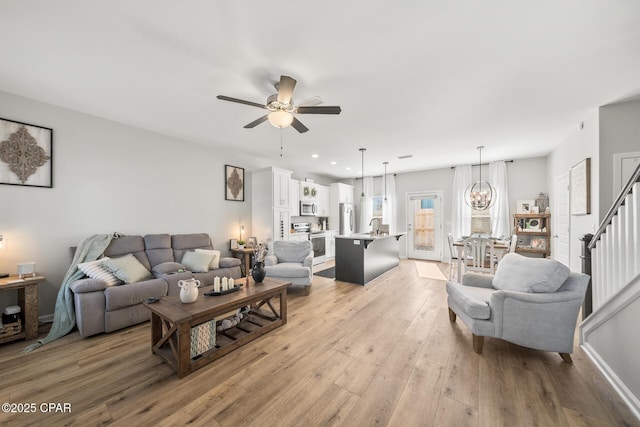 living room with ceiling fan with notable chandelier, sink, and light hardwood / wood-style floors