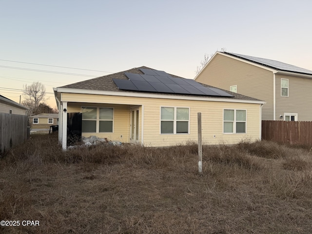 6610 Boat Race Rd, Panama City, FL 32404 - back of property at dusk featuring roof mounted solar panels, fence, and roof with shingles
