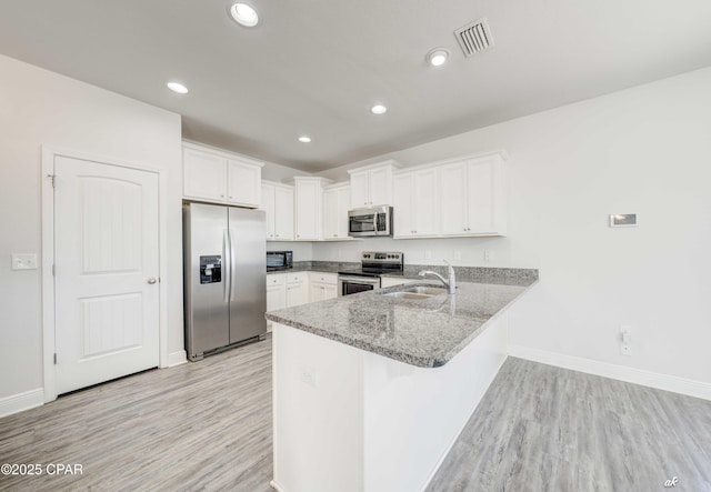 kitchen featuring appliances with stainless steel finishes, white cabinetry, sink, light hardwood / wood-style floors, and kitchen peninsula