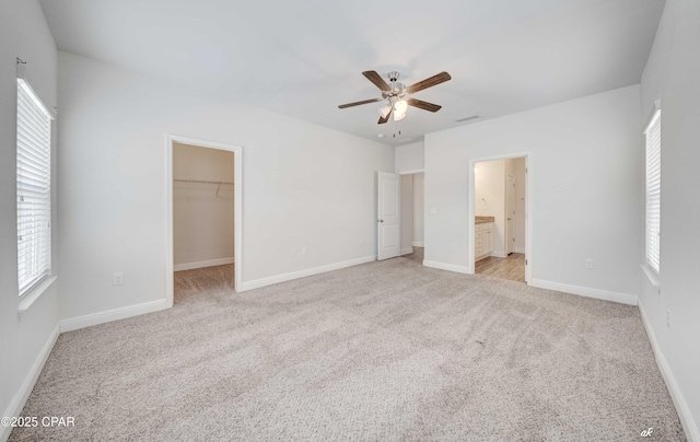 unfurnished bedroom with a walk in closet, ensuite bath, light colored carpet, a closet, and ceiling fan