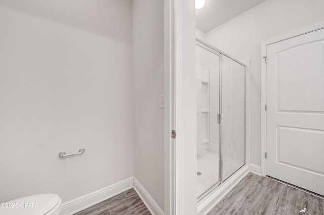 bathroom featuring wood-type flooring, a shower with door, and toilet