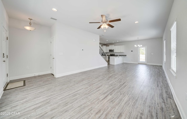 unfurnished living room featuring ceiling fan with notable chandelier and light hardwood / wood-style flooring