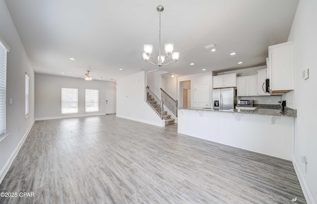 kitchen featuring decorative light fixtures, kitchen peninsula, stone counters, stainless steel appliances, and white cabinets