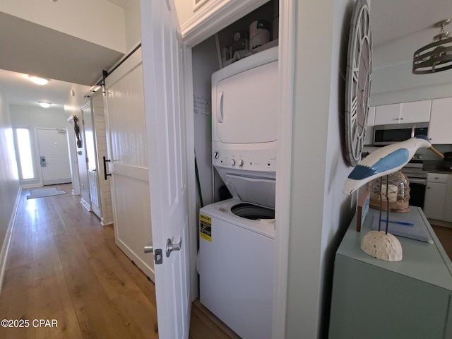 laundry room featuring stacked washer / drying machine, a barn door, and light wood-type flooring