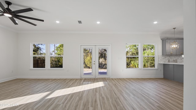 unfurnished living room featuring ornamental molding, ceiling fan with notable chandelier, and light wood-type flooring