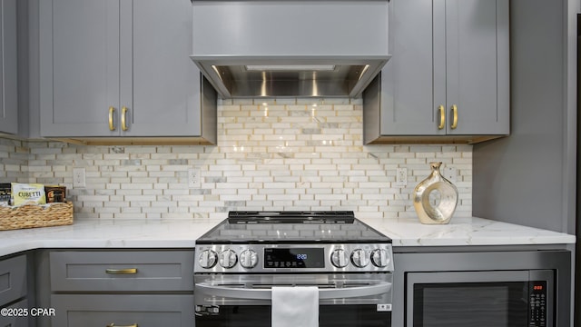 kitchen with gray cabinetry, backsplash, premium range hood, and appliances with stainless steel finishes