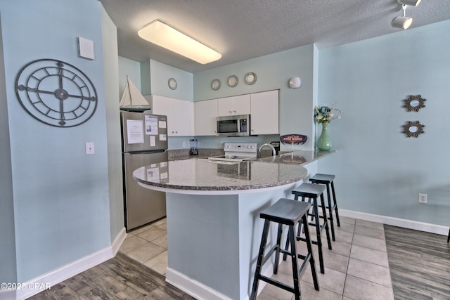 kitchen with white cabinetry, stainless steel appliances, a kitchen bar, kitchen peninsula, and dark stone counters