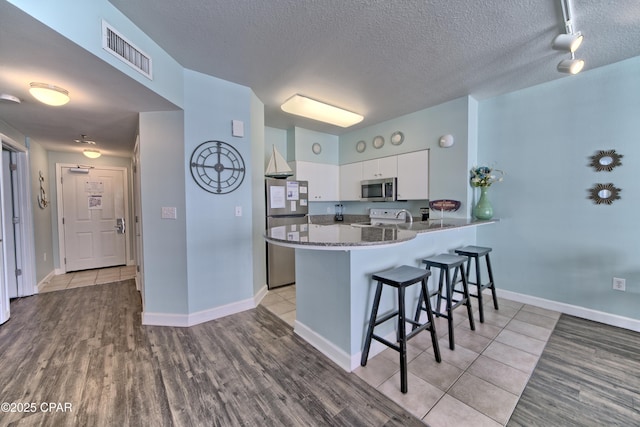 kitchen with appliances with stainless steel finishes, white cabinets, a kitchen breakfast bar, light hardwood / wood-style floors, and kitchen peninsula