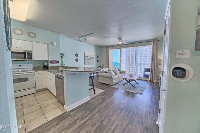 kitchen with a breakfast bar, rail lighting, white cabinets, kitchen peninsula, and stainless steel appliances