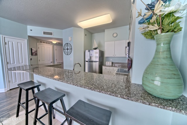 kitchen with a textured ceiling, stainless steel fridge, kitchen peninsula, and white cabinets