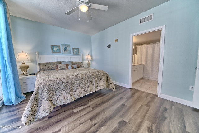 bedroom with ceiling fan, connected bathroom, a textured ceiling, and light wood-type flooring