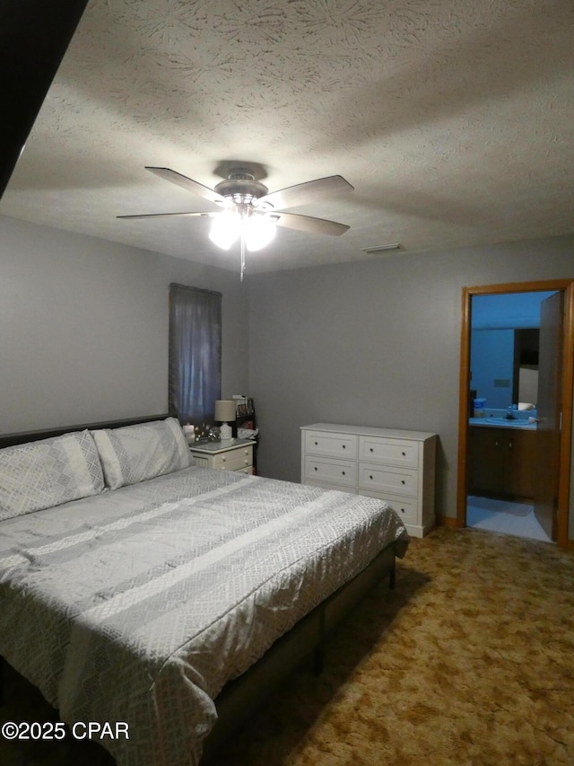 bedroom with ceiling fan, ensuite bathroom, carpet floors, and a textured ceiling