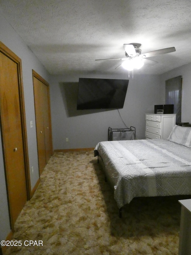 carpeted bedroom featuring ceiling fan, two closets, and a textured ceiling