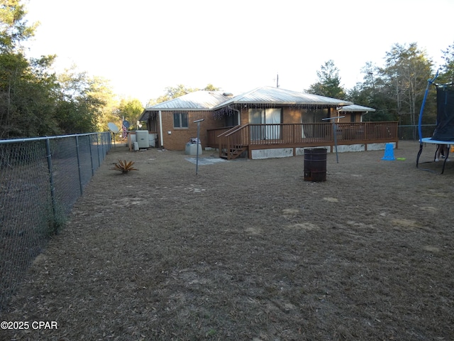 back of property with a wooden deck and a trampoline