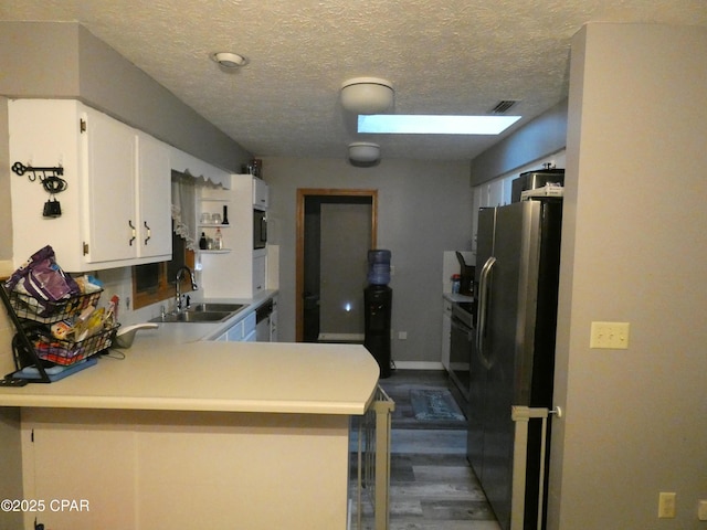 kitchen featuring sink, stainless steel appliances, a textured ceiling, white cabinets, and kitchen peninsula