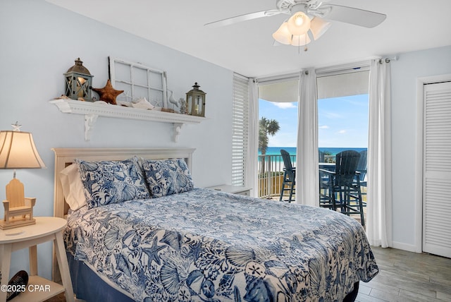 bedroom with a water view, a wall of windows, light hardwood / wood-style flooring, access to outside, and ceiling fan