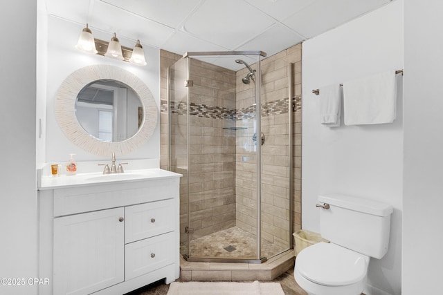 bathroom featuring vanity, a shower with shower door, a drop ceiling, and toilet