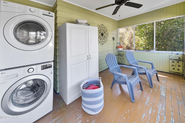 laundry area featuring ceiling fan, stacked washer / drying machine, hardwood / wood-style floors, and wooden walls