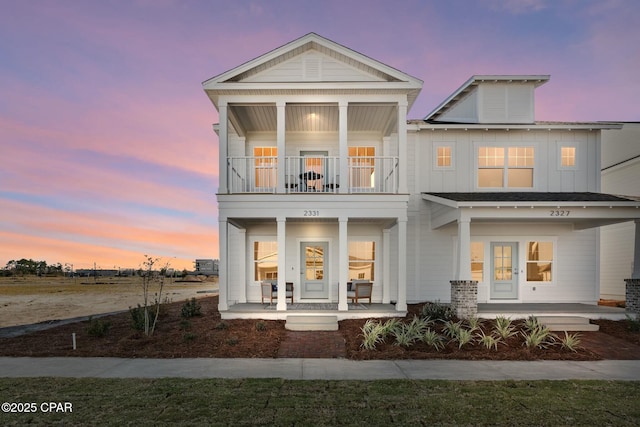 back house at dusk with french doors, a balcony, and covered porch