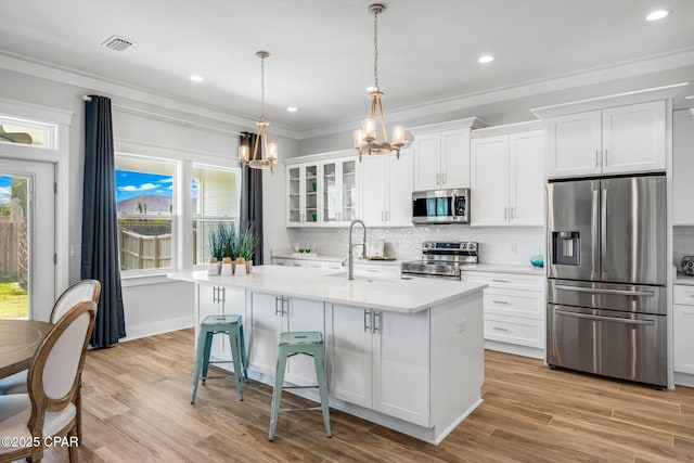 kitchen with white cabinetry, ornamental molding, an island with sink, pendant lighting, and stainless steel appliances