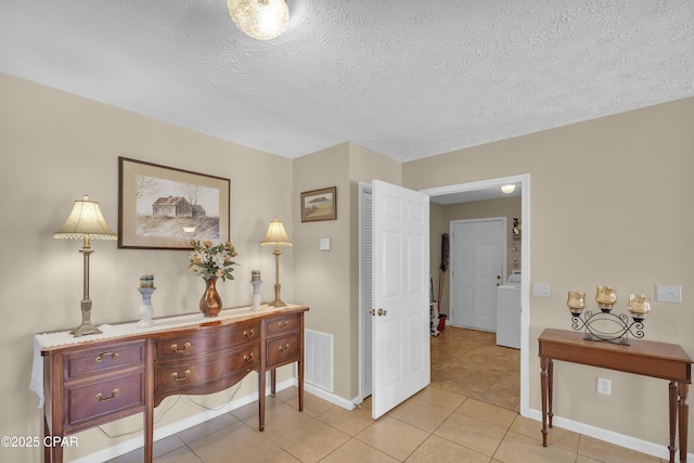 hall featuring washer / dryer, light tile patterned floors, and a textured ceiling