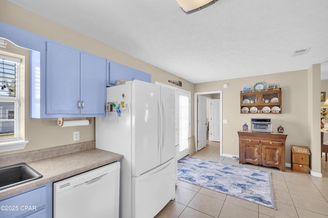 kitchen with blue cabinets, sink, a textured ceiling, light tile patterned floors, and white appliances