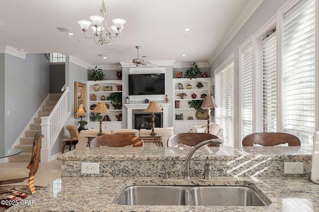 kitchen featuring ceiling fan with notable chandelier, decorative light fixtures, sink, ornamental molding, and light stone countertops