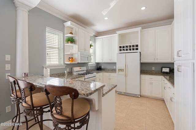 kitchen featuring dark stone countertops, white cabinets, light tile patterned floors, kitchen peninsula, and white appliances