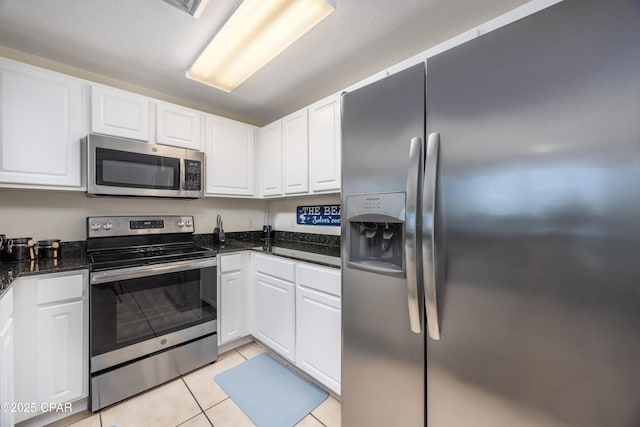 kitchen featuring stainless steel appliances, white cabinetry, light tile patterned floors, and dark stone counters