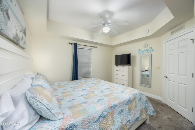 bedroom with a raised ceiling, carpet flooring, and ceiling fan