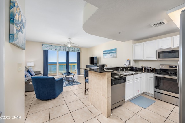 kitchen with light tile patterned floors, sink, appliances with stainless steel finishes, white cabinets, and kitchen peninsula