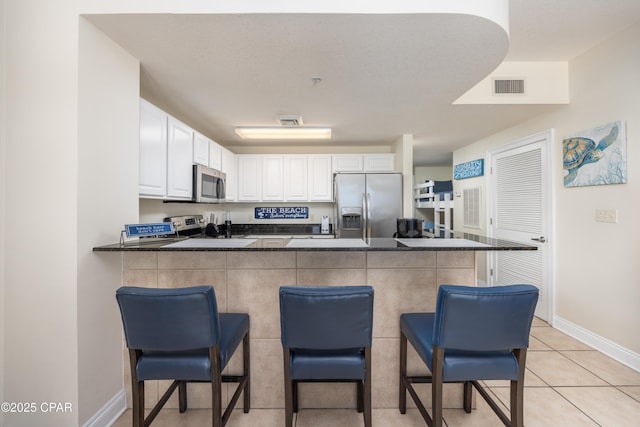 kitchen with a breakfast bar, appliances with stainless steel finishes, white cabinetry, light tile patterned flooring, and kitchen peninsula