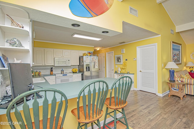 kitchen with lofted ceiling with beams, kitchen peninsula, white cabinets, white appliances, and backsplash