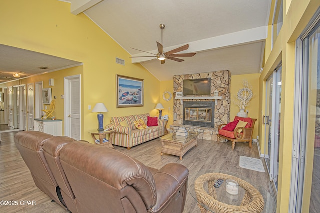 living room with ceiling fan, a stone fireplace, light hardwood / wood-style floors, and vaulted ceiling with beams