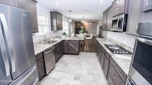 kitchen featuring dark brown cabinets, light stone countertops, a peninsula, stainless steel appliances, and a sink