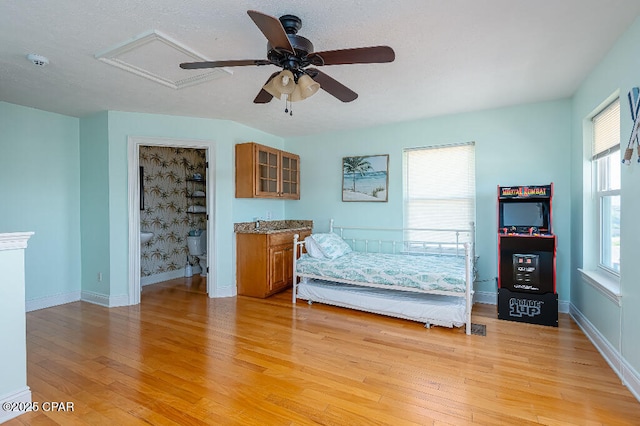 unfurnished bedroom with attic access, light wood-style floors, baseboards, and ceiling fan