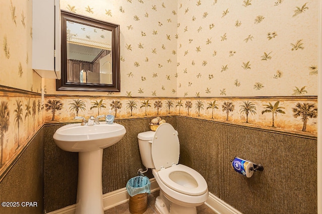 bathroom with toilet, wainscoting, and wallpapered walls