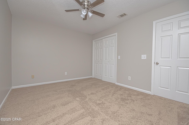 unfurnished bedroom featuring ceiling fan, light colored carpet, a textured ceiling, and a closet