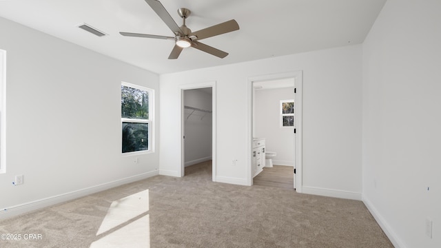 unfurnished bedroom with light colored carpet, ensuite bathroom, a spacious closet, and multiple windows