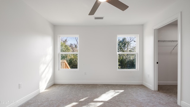 unfurnished bedroom featuring multiple windows, a walk in closet, light colored carpet, and a closet