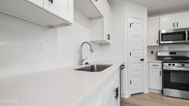 kitchen with sink, light hardwood / wood-style flooring, stainless steel appliances, decorative backsplash, and white cabinets