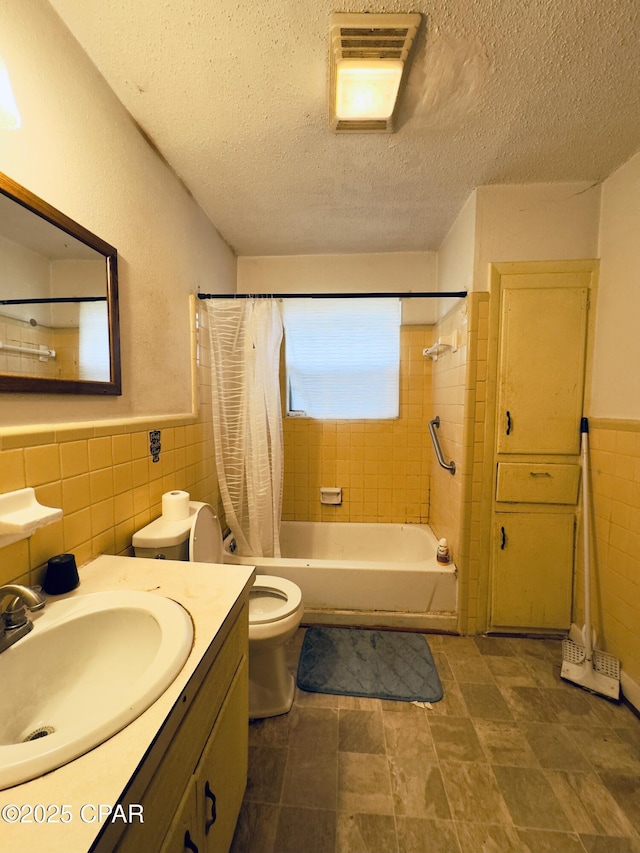 full bathroom with shower / tub combo with curtain, tile walls, vanity, toilet, and a textured ceiling