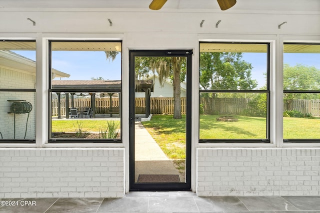 doorway to outside with ceiling fan and brick wall