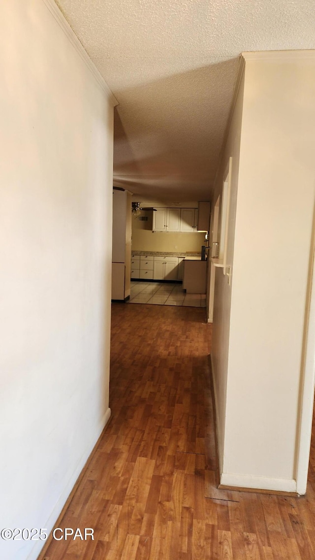 hallway with hardwood / wood-style flooring, crown molding, and a textured ceiling