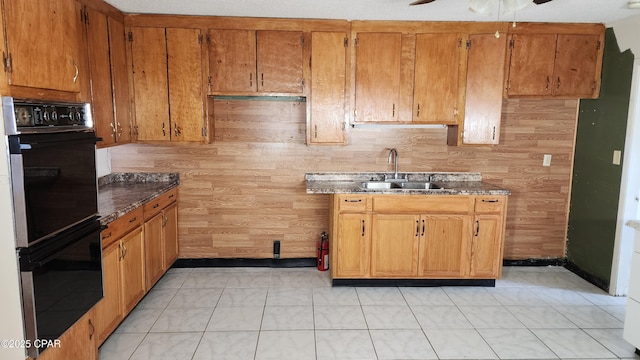 kitchen with light tile patterned floors, sink, ceiling fan, double oven, and wood walls